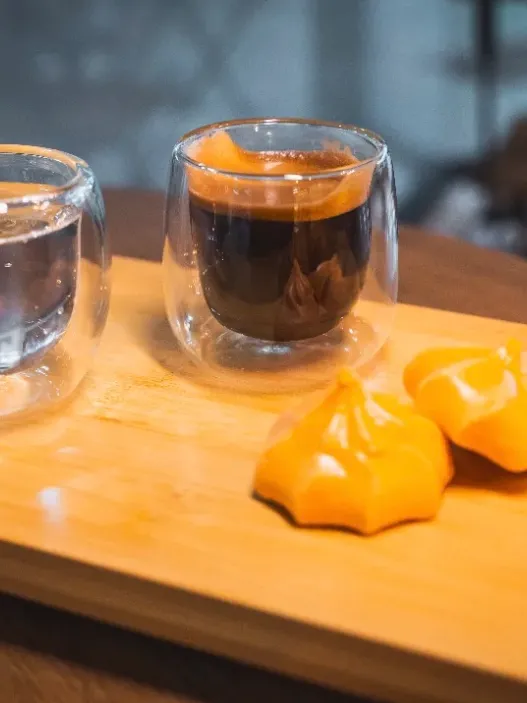 Espresso en vaso de vidrio con merengues sobre una bandeja de madera